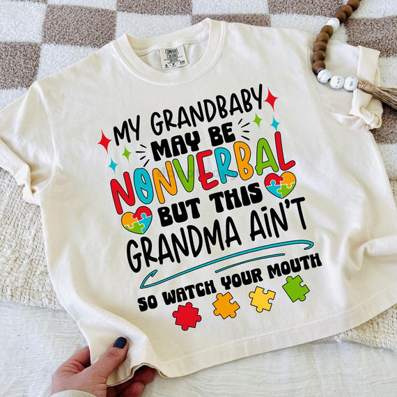 My Grandbaby Maybe Nonverbal But This Grandma Ain't DTF Heat Transfer, t-shirt with colorful text and puzzle piece designs highlighting grandma's support for her nonverbal grandchild.