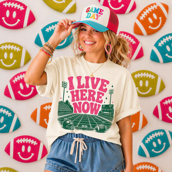I Live Here Now Football Field DTF Heat Transfer, colorfully designed football-themed graphic on a person’s t-shirt with a playful background of footballs with smiley faces.