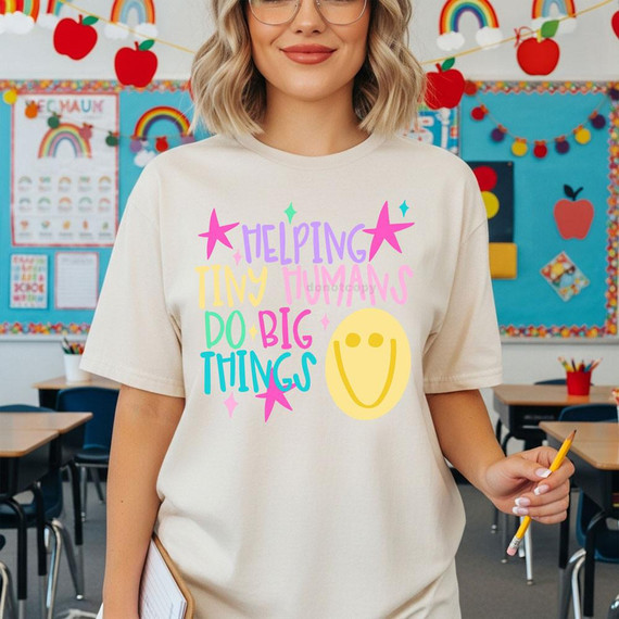 Helping Tiny Humans Do Big Things DTF Heat Transfer, colorful graphic t-shirt worn by a woman in a classroom.