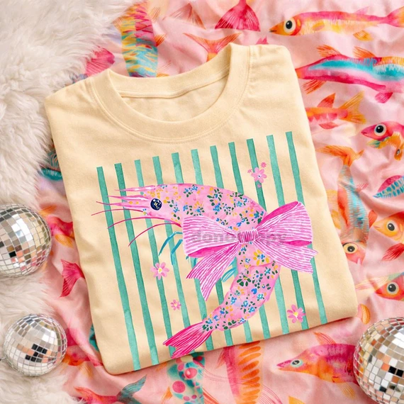 Coquette Shrimp DTF Heat Transfer, colorful shrimp design on a beige t-shirt with striped background, vibrant and eye-catching.