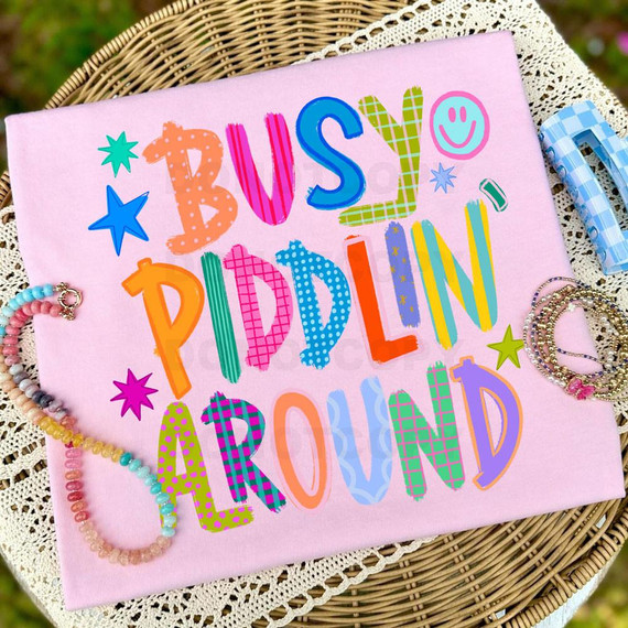 Busy Piddlin' Around DTF Heat Transfer, colorful and playful design on a pink fabric background with jewelry and craft supplies around it.