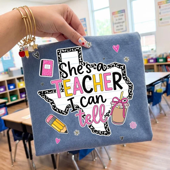 She's a Teacher I Can Tell Texas DTF Heat Transfer on a classroom tote bag, featuring colorful and playful design elements with school-related icons like a notebook, pencil, and a drink with a pink bow.
