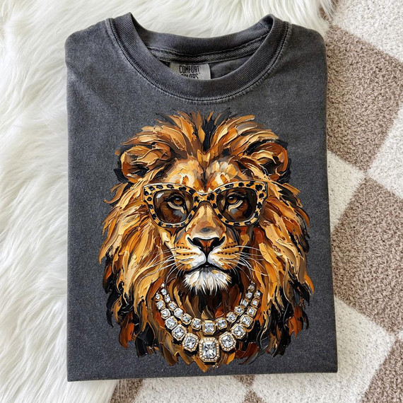 Glam Lion DTF Transfer, a printed design of a lion wearing fashionable glasses and jewelry, on a folded gray t-shirt.
