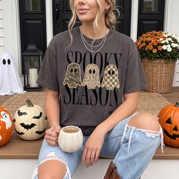 Spooky Season Ghosts DTF Heat Transfer, Halloween-themed ghost illustrations with camouflage, leopard, and checkered patterns on a woman's T-shirt promoting Halloween festivities.