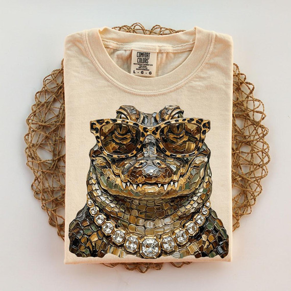 Glam Alligator DTF Heat Transfer, a detailed illustration of an alligator wearing sunglasses and a diamond necklace on a beige T-shirt.