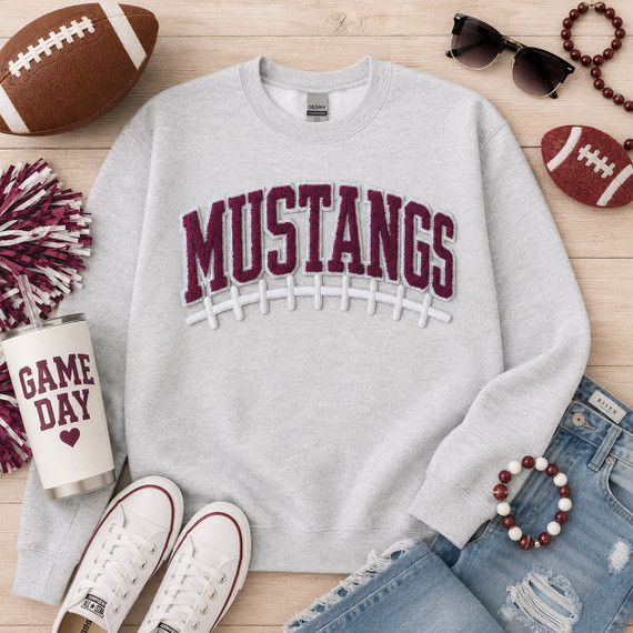Maroon Mustangs chenille football apparel patch with sequin outline and white embroidered football laces displayed on a gray sweatshirt