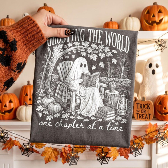 Ghosting the World One Chapter at a Time DTF Transfer, cozy fall ghost reading design on a fabric, surrounded by Halloween decorations including pumpkins, ghost figures, and spider webs for seasonal decor.