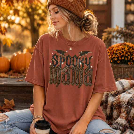 Spooky Mama DTF transfer with gothic lettering, leopard print fill, bat wings, and stars on a rust colored t-shirt