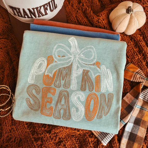 Pumpkin Season DTF Transfer, Retro Bow Fall Design on a fabric, surrounded by fall decor items like a small pumpkin, a thankful sign, and plaid fabric, for seasonal craft or clothing decoration.