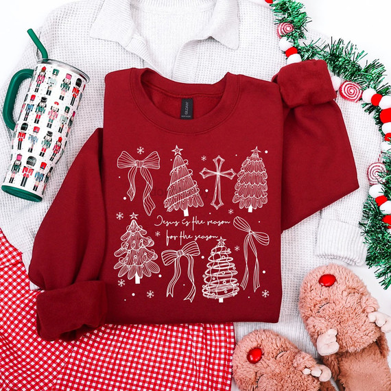 Jesus Is the Reason for the Season Christmas DTF transfer with hand-drawn white line art trees, bows, and a cross on a garnet sweatshirt