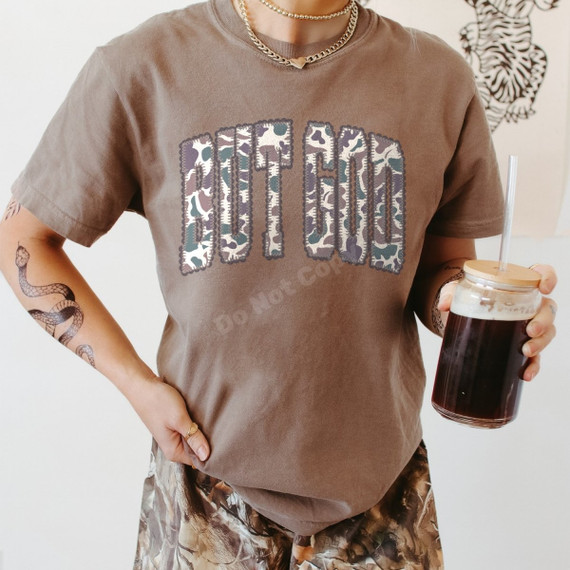 But God DTF transfer with bold camo patch-style lettering on a brown t-shirt