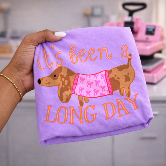 It's Been a Long Day DTF transfer featuring a brown dachshund in a pink bow-print pajama shirt, hand-lettered in orange script