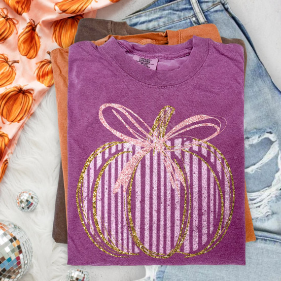 Pink and gold glitter-inspired striped pumpkin DTF transfer with bow accent on a purple shirt