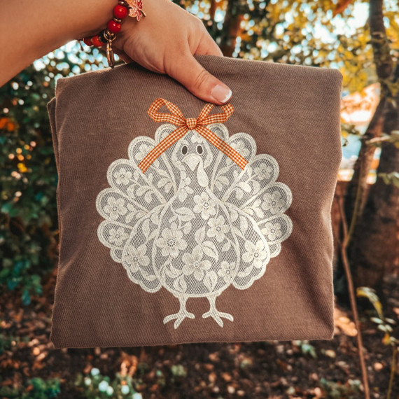 Lace-style turkey DTF transfer with floral lace pattern and gingham bow on a brown shirt
