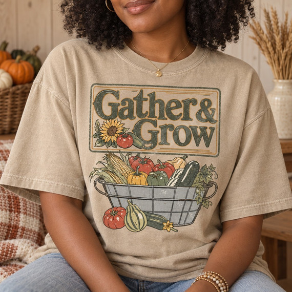 Gather & Grow DTF transfer with vintage sign-style lettering, sunflower, and wire basket overflowing with corn, tomatoes, peppers and squash Shown on a Sandstone t-shirt.