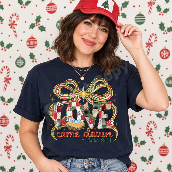 Love Came Down nativity DTF transfer with patchwork-style LOVE lettering, baby Jesus in a manger, a red green and gold ribbon bow, starburst, and Luke 2:11 scripture citation Shown on a True Navy t-shirt.