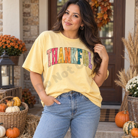 THANKFUL arched varsity letters in distressed vintage multicolor with black outlines on a mustard yellow t-shirt Shown on a Butter t-shirt.