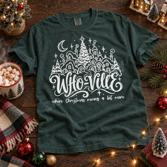Who-Ville Christmas DTF transfer with white linework snowy village, decorated tree, crescent moon, stars, and the phrase 'where Christmas means a bit more' in cursive lettering Shown on a Blue Spruce t-shirt.