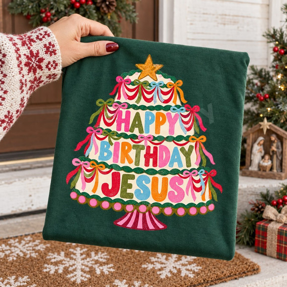 Happy Birthday Jesus DTF transfer featuring a folk-art Christmas tree-shaped cake with garlands, bows, a gold star topper, and rainbow lettering Shown on a Emerald t-shirt.