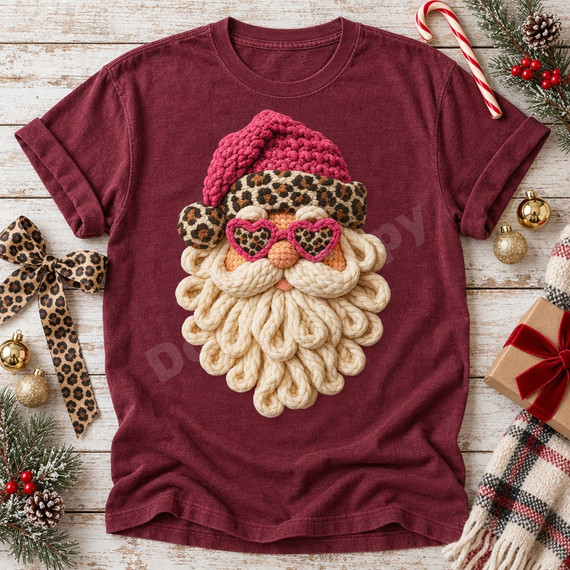 Whimsical crocheted-look Santa face DTF transfer with hot pink knit hat, leopard print headband and earmuffs, pink heart-shaped leopard sunglasses, and a looped cream yarn beard Shown on a Wine t-shirt.