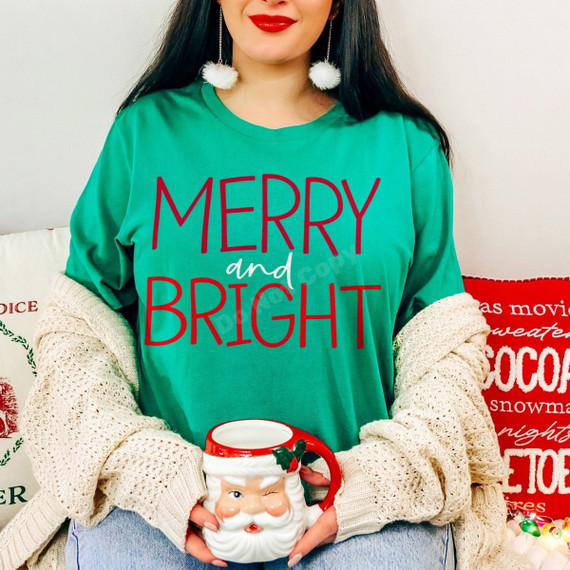 Merry and Bright DTF transfer in bold red lettering with a white script 'and' accent, shown on a green Christmas shirt