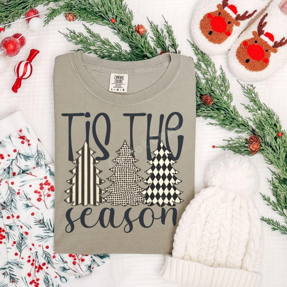 Tis the Season DTF Transfer | Patterned Christmas Trees Design, festive lettering and three patterned Christmas trees printed on a folded sage green sweatshirt, styled with holiday greenery and cozy winter accessories.