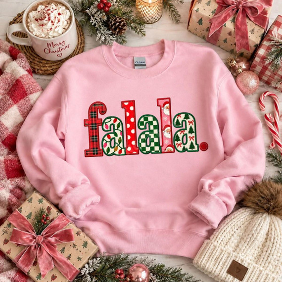 Falala Christmas DTF Transfer | Faux Embroidery Holiday Lettering Design, festive “falala” lettering in red and green Christmas patterns displayed on a pink sweatshirt surrounded by holiday gifts and decorations.