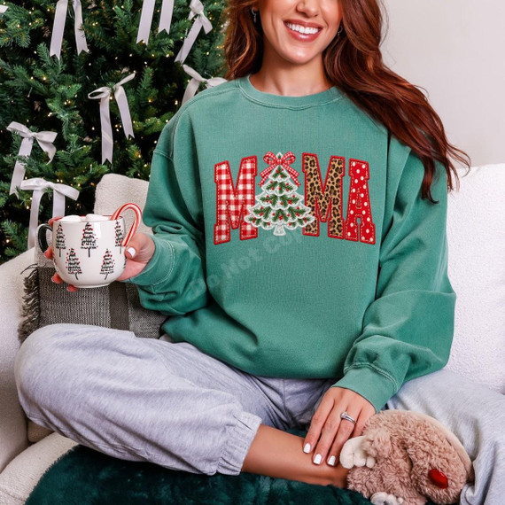 Mama Christmas DTF Transfer | Faux Embroidered Plaid & Leopard Design, faux embroidered red plaid and leopard print “MAMA” Christmas tree design displayed on a teal sweatshirt worn by a woman beside a decorated Christmas tree