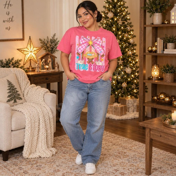 True Story Nativity DTF Transfer | Pink Gingham Christmas Manger Design, woman modeling a pink T-shirt featuring a colorful nativity scene with a pink gingham bow and “True Story” lettering in a festive Christmas living room.