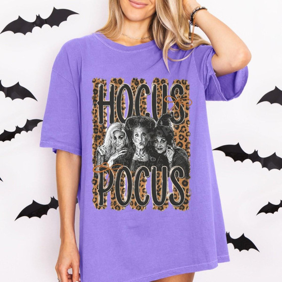 Hocus Pocus Witches DTF Transfer | Leopard Print Halloween Design, leopard-print Hocus Pocus graphic featuring three witches on a purple T-shirt modeled against a Halloween bat backdrop.