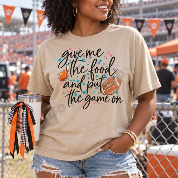 Give Me the Food and Put the Game On DTF Transfer | Funny Football Game Day Design, colorful script football and food graphic displayed on a beige T-shirt at a stadium