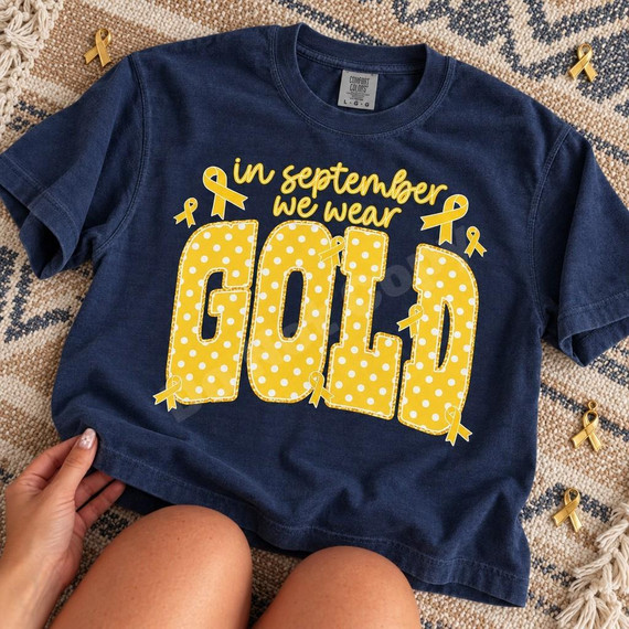 In September We Wear Gold DTF Transfer | Childhood Cancer Awareness Design, gold polka-dot lettering and awareness ribbons displayed on a navy blue T-shirt