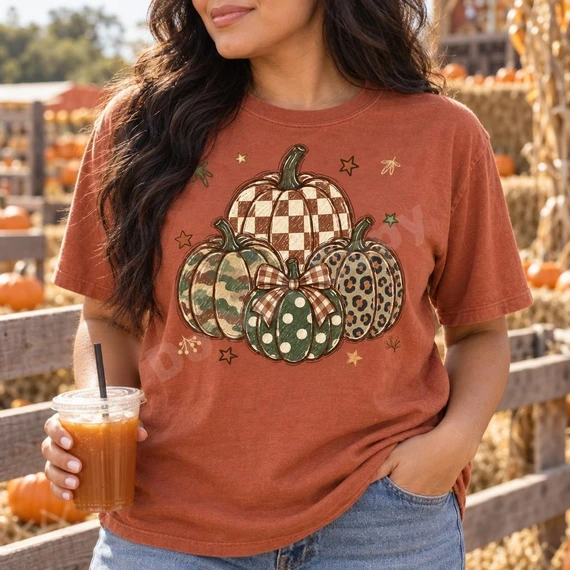Patterned Pumpkin Stack DTF Transfer | Hand-Sketched Autumn Design, hand-sketched stack of pumpkins in assorted fall patterns printed on a rust-colored T-shirt, modeled at a pumpkin patch