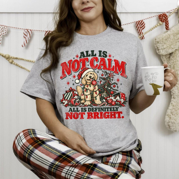 All Is Not Calm Christmas Dog DTF Transfer | Funny Holiday Design, festive graphic of a Santa-hat dog tangled in Christmas lights among holiday presents with the phrase “All Is Not Calm, All Is Definitely Not Bright,” shown on a gray T-shirt.