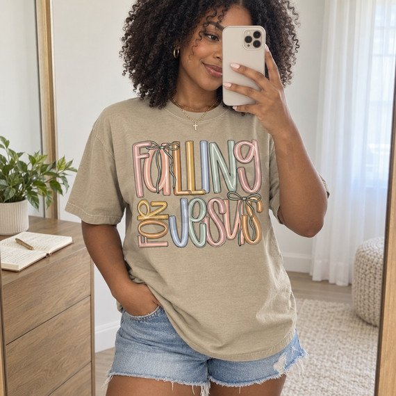 Falling for Jesus DTF transfer in bold hand-lettered multicolor typography with pastel blush, mustard, dusty blue, and sage tones, accented with sage green bow ribbons Shown on a Hemp t-shirt.