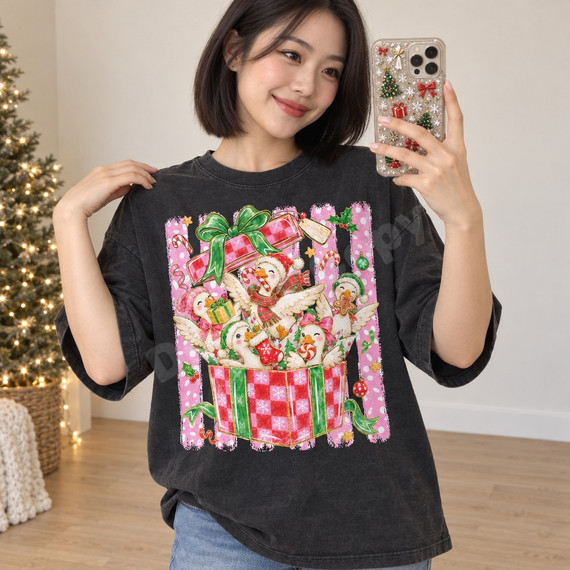 Whimsical Christmas ducks DTF transfer featuring five fluffy ducks in Santa hats and scarves popping out of a checkered gift box with candy canes and holly Shown on a Pepper t-shirt.