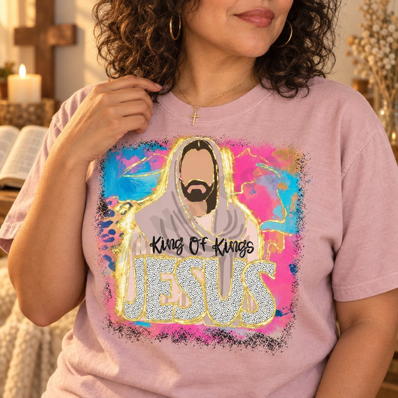 King Of Kings Jesus DTF transfer featuring a faceless Jesus portrait in a flowing robe over a pink, blue, and gold abstract watercolor background with gold foil-style outlining Shown on a Rose Quartz t-shirt.