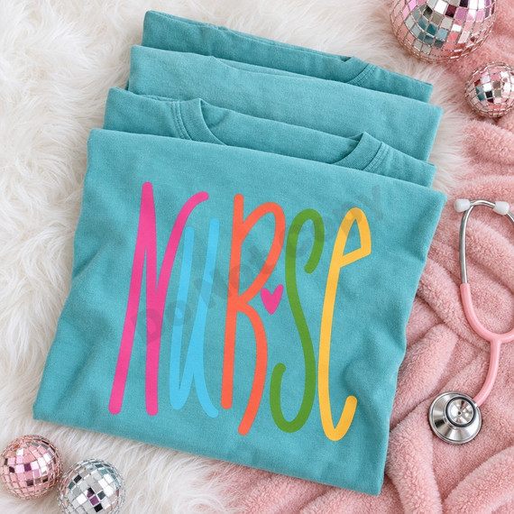 NURSE DTF transfer hand-lettered in tall rainbow-colored strokes with a small pink heart accent between the letters Shown on a Island Reef t-shirt.