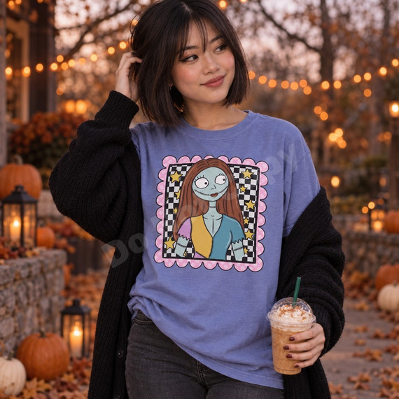 Blue-skinned ragdoll girl Halloween DTF transfer with auburn hair and patchwork top in a checkered frame with pink scalloped border and gold stars Shown on a Periwinkle t-shirt.