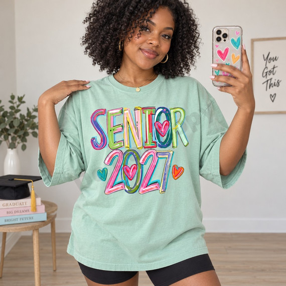 Senior 2027 DTF transfer in hand-painted graffiti-style rainbow lettering with black outlines and scattered doodle hearts Shown on a Seafoam t-shirt.