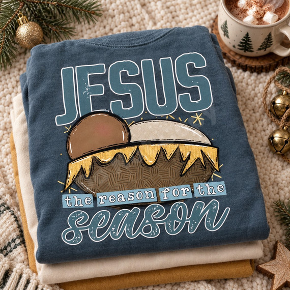Jesus the reason for the season DTF transfer with bold vintage JESUS lettering and illustrated manger with baby Jesus in golden straw Shown on a Mystic Blue t-shirt.