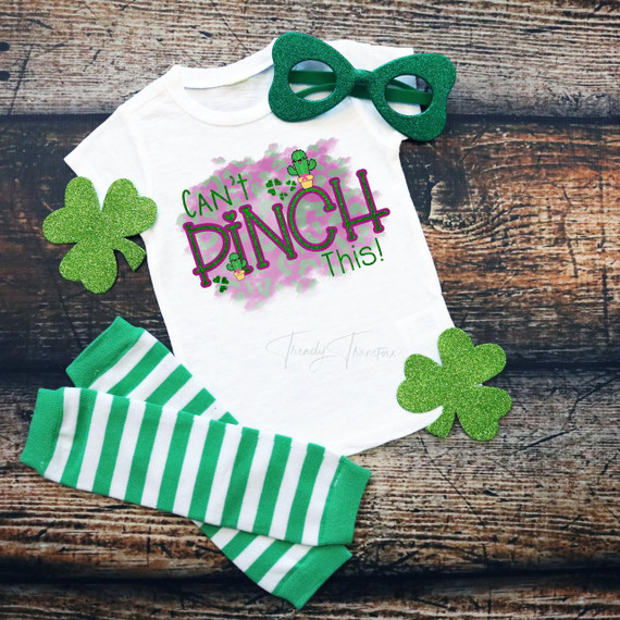 Can't pinch this St. Patrick's Day Sublimation Transfer, a colorful design on a white T-shirt with green and purple lettering and shamrocks, surrounded by green striped socks, green glitter shamrocks, and green glasses for St. Patrick's Day celebration.