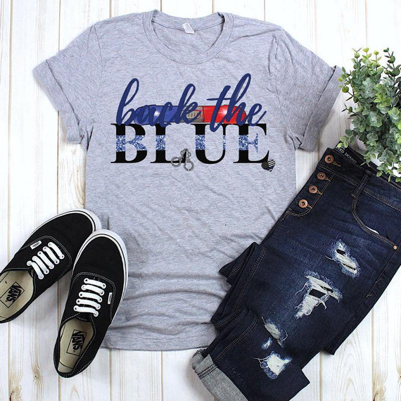 Back The Blue Screen Print Heat Transfer, gray t-shirt with 'back the blue' text design, paired with distressed jeans, black sneakers, and a green plant for display.