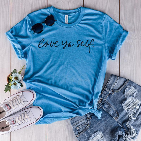 Love Yo Self Screen Print Transfer, blue T-shirt with black script lettering and casual denim shorts, with accessories like white sneakers, sunglasses, and a small bouquet of flowers.