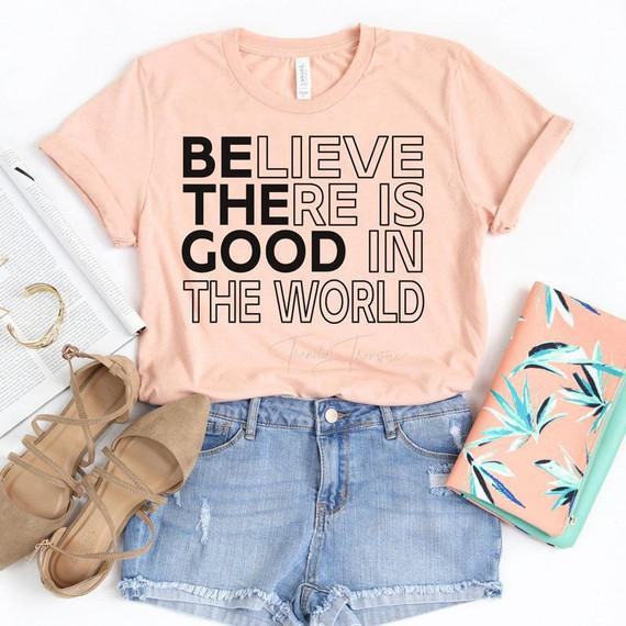 Believe There Is Good In The World Screen Print Transfer, peach T-shirt with bold black and outlined text, paired with denim shorts, beige heels, and floral planner for casual style.