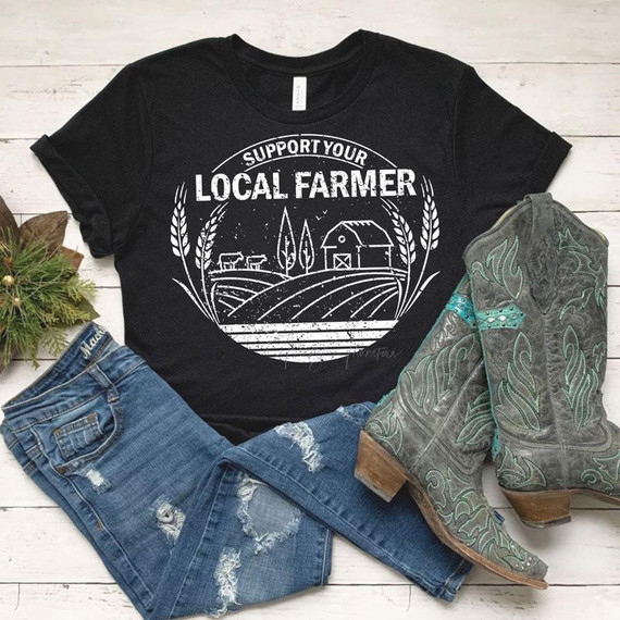 Support Your Local Farmer White Screen Print Transfer T-shirt, casual black t-shirt with a farm-themed design, distressed blue jeans, and cowboy boots with green and gray patterns, on a white wooden background.