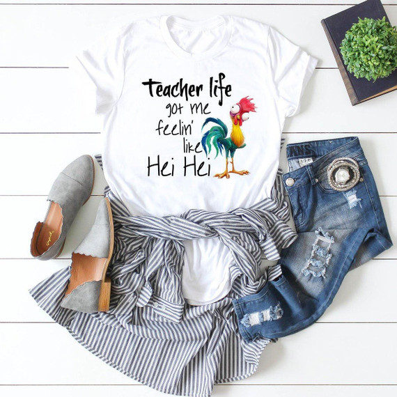 Teacher Life Got Me Feelin' Like Hei Hei Sublimation Transfer, a white t-shirt with a humorous graphic of Hei Hei the rooster from Moana, laid out on a white wooden surface with denim jeans, gray shoes, a striped shirt, and decorative plant nearby.