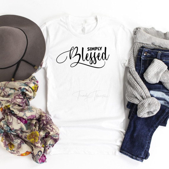 Simply Blessed Sublimation Transfer, a white T-shirt with black decorative text, placed among a gray hat, a floral scarf, and a pair of jeans with a gray knit sweater, showcasing vibrant clothing accessories.