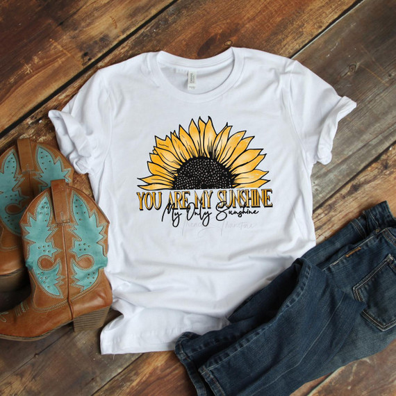 You Are My Sunshine Sunflower Sublimation Transfer, white t-shirt with sunflower design and text, paired with cowboy boots and jeans, on wooden surface