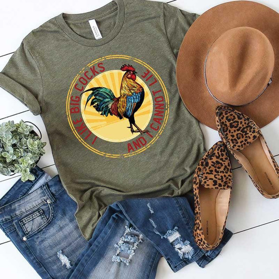 I Like Big Cocks Screen Print Heat Transfer T-shirt, casual olive-green T-shirt with colorful rooster graphic and circular text design, paired with distressed denim shorts, leopard print heels, and a brown wide-brim hat.